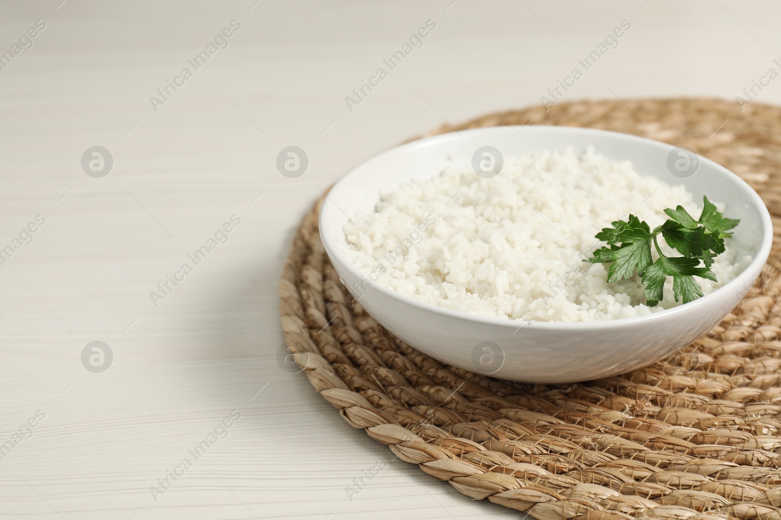 Photo of Delicious boiled rice in bowl and parsley on wooden table, space for text