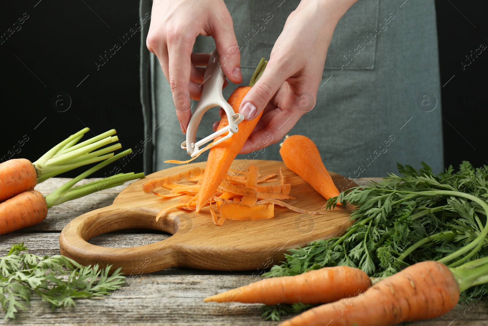 Photo of Woman peeling fresh carrot at wooden table, closeup