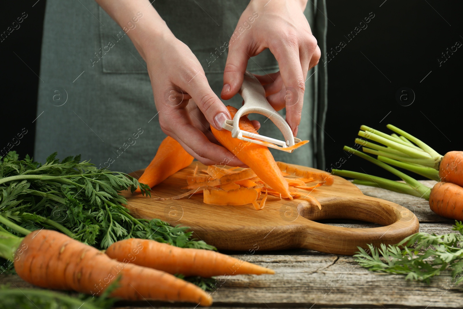 Photo of Woman peeling fresh carrot at wooden table, closeup