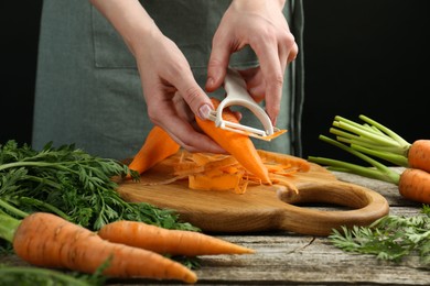 Photo of Woman peeling fresh carrot at wooden table, closeup