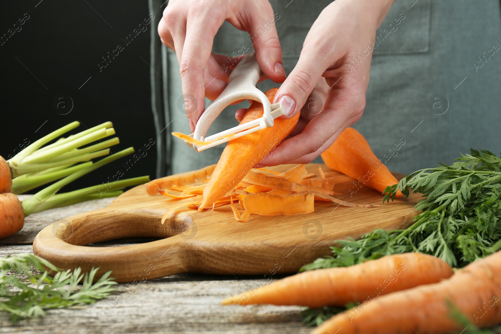 Photo of Woman peeling fresh carrot at wooden table, closeup