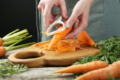 Photo of Woman peeling fresh carrot at wooden table, closeup