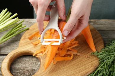 Photo of Woman peeling fresh carrot at wooden table, closeup