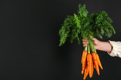 Photo of Woman holding ripe carrots on black background, closeup. Space for text