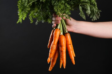 Photo of Woman holding ripe carrots on black background, closeup. Space for text