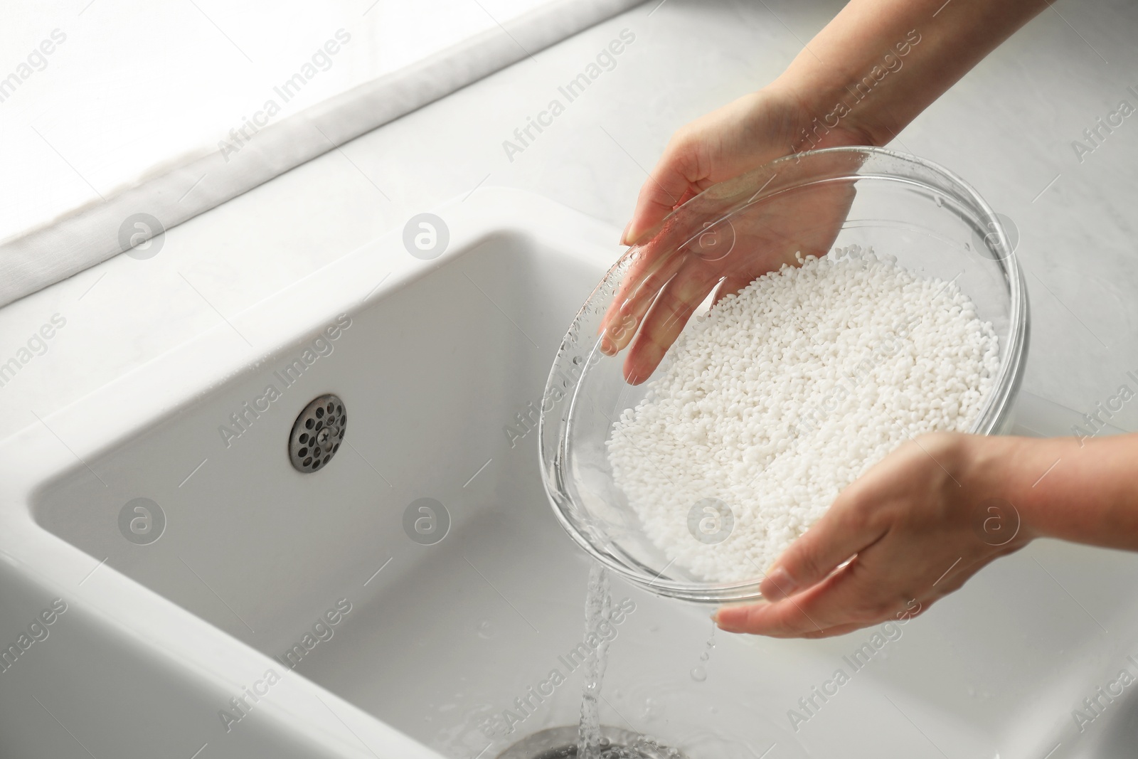 Photo of Woman rinsing rice in bowl above sink, closeup