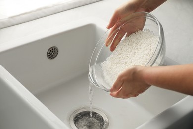 Photo of Woman rinsing rice in bowl above sink, closeup