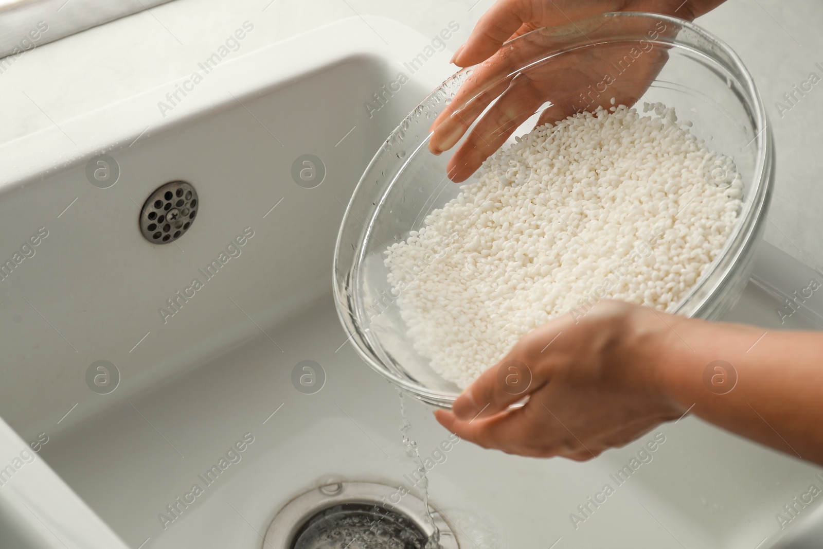 Photo of Woman rinsing rice in bowl above sink, closeup