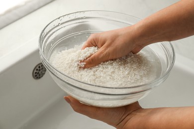 Photo of Woman rinsing rice in bowl above sink, closeup