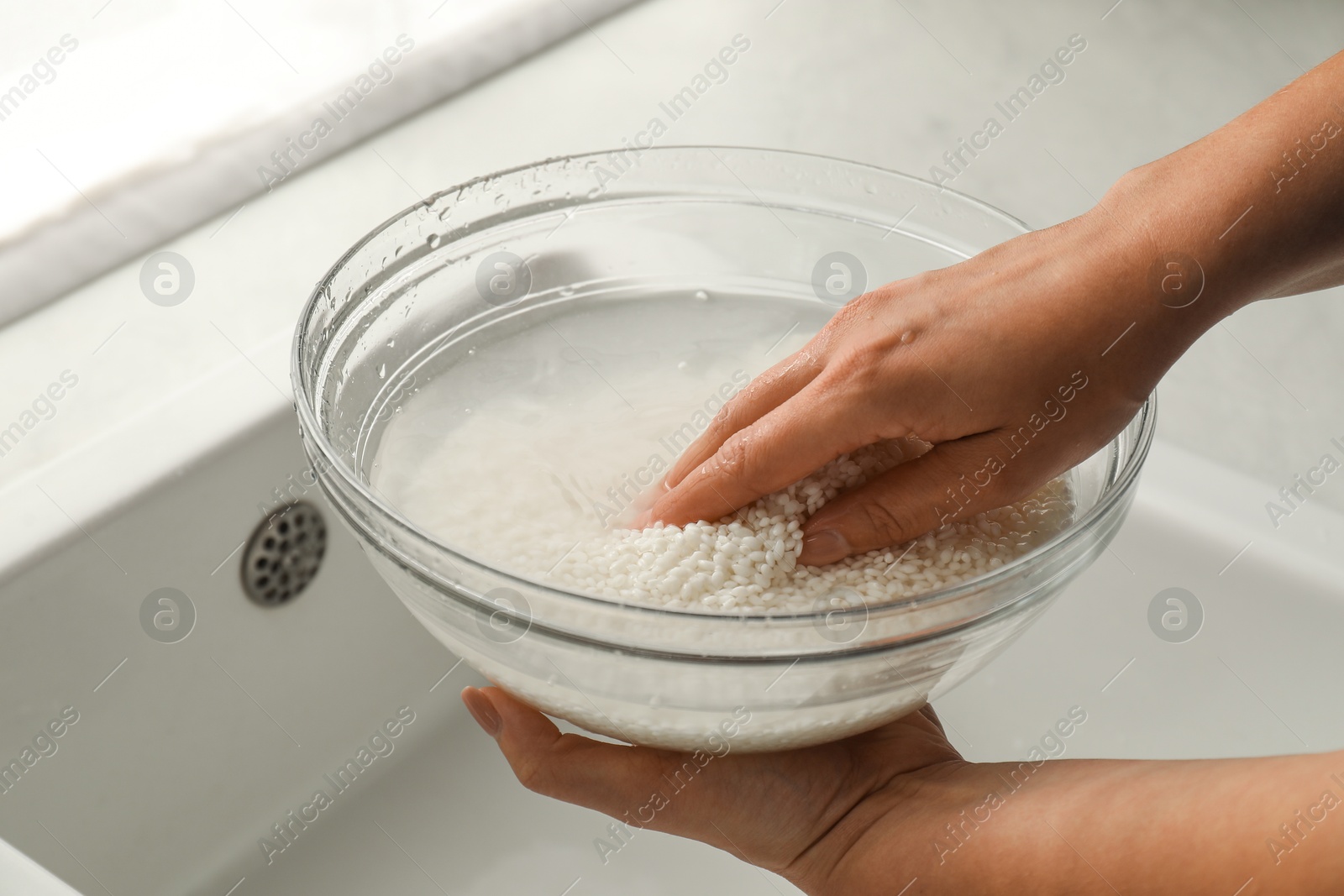 Photo of Woman rinsing rice in bowl above sink, closeup