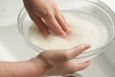 Photo of Woman rinsing rice in bowl above sink, closeup