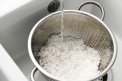 Photo of Pouring water into colander with rice in sink, closeup