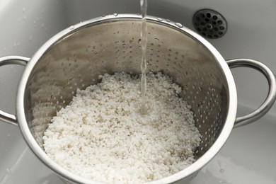 Photo of Pouring water into colander with rice in sink, closeup