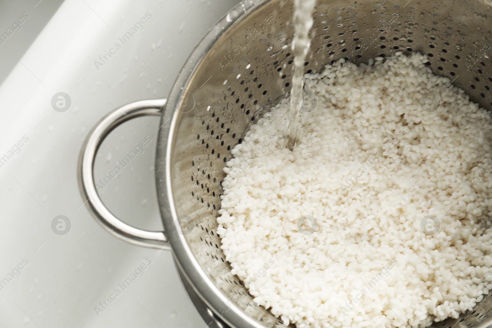 Photo of Pouring water into colander with rice in sink, closeup