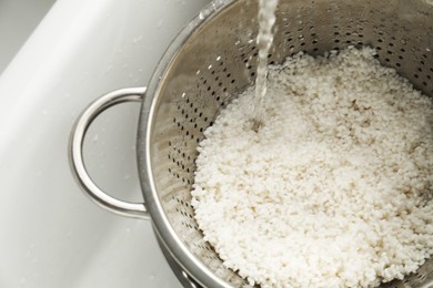 Photo of Pouring water into colander with rice in sink, closeup