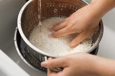 Photo of Woman rinsing rice in colander at sink, closeup