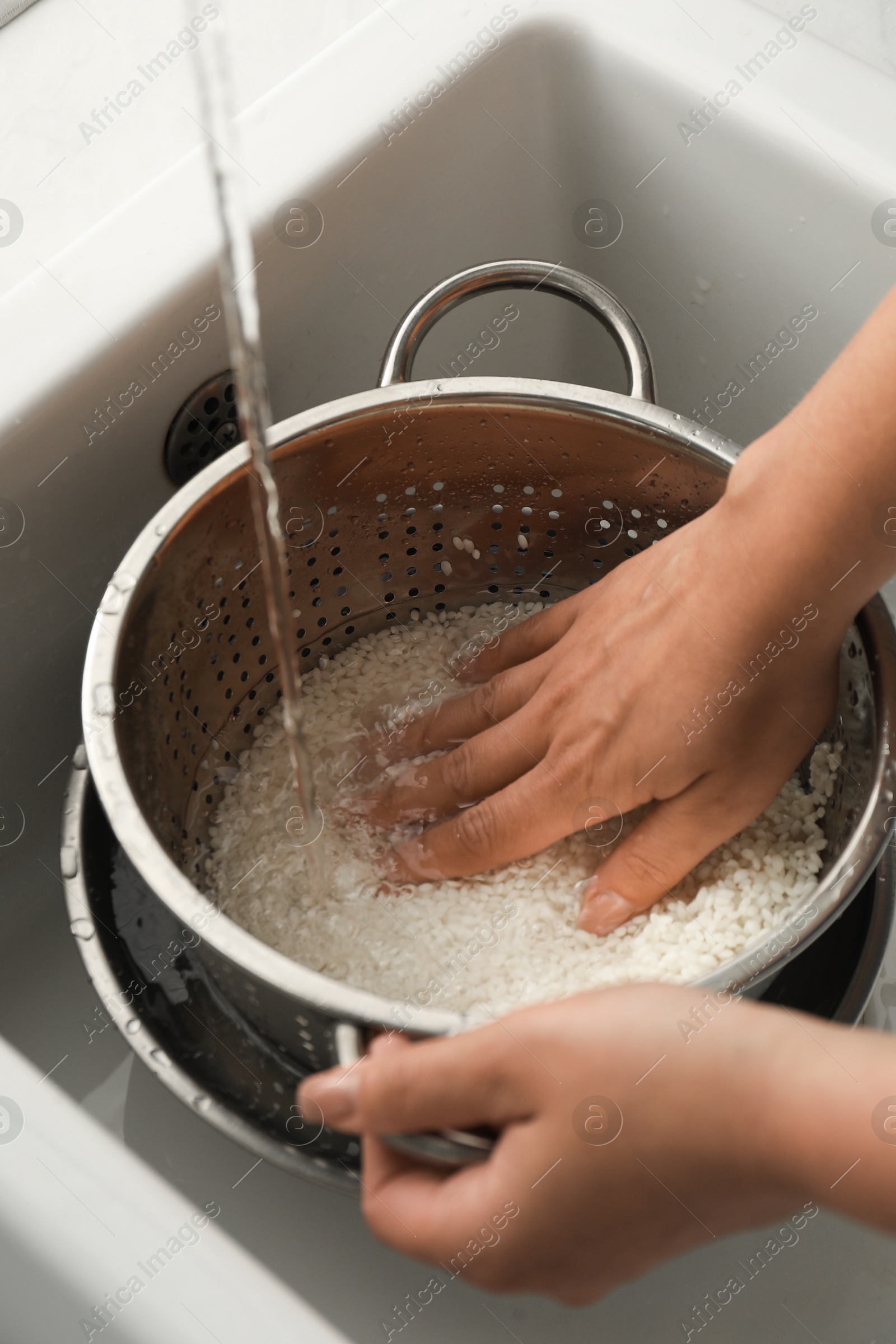 Photo of Woman rinsing rice in colander at sink, closeup