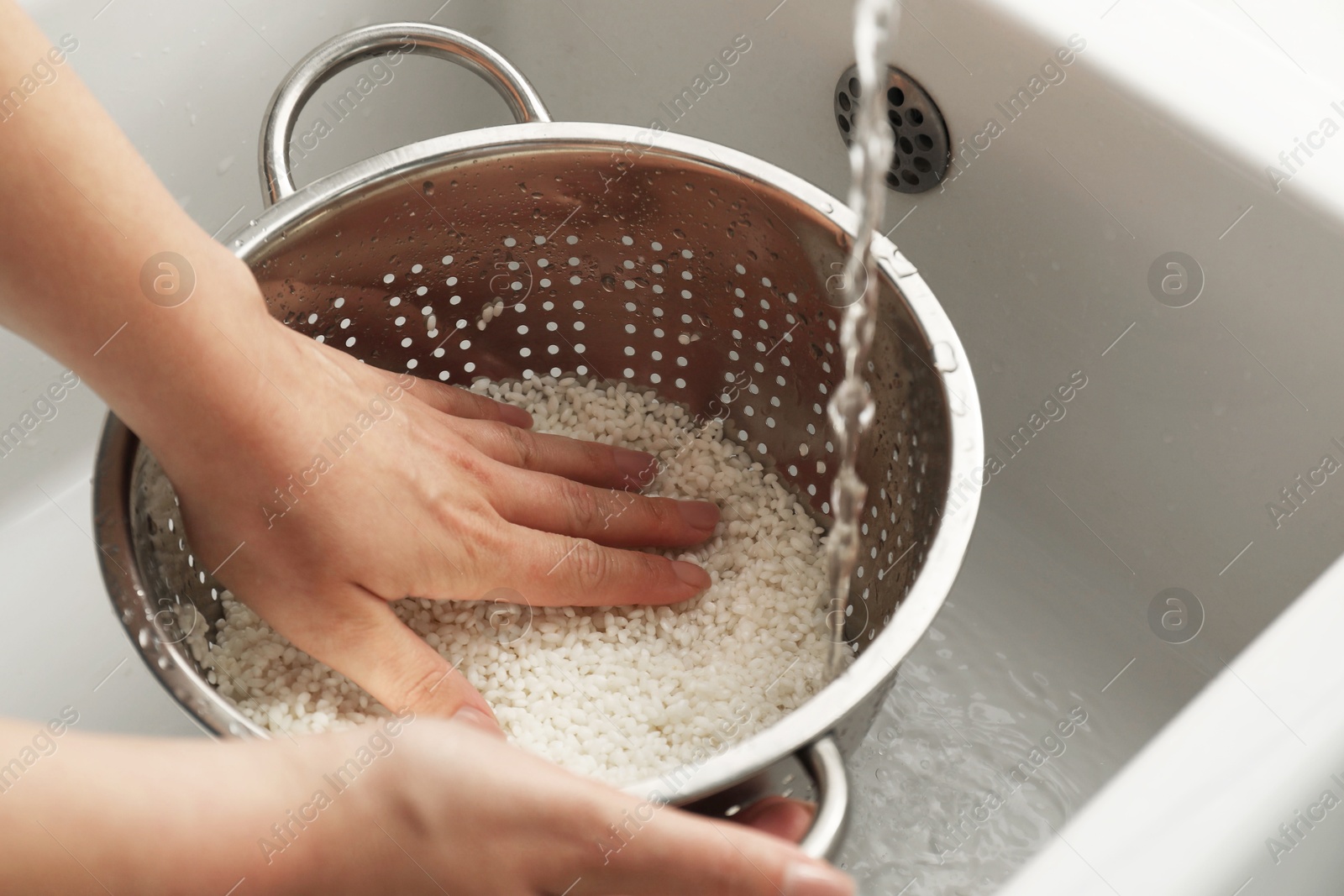 Photo of Woman rinsing rice in colander at sink, closeup