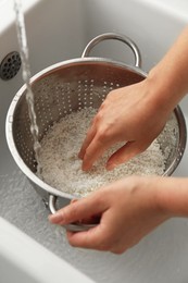 Photo of Woman rinsing rice in colander at sink, closeup