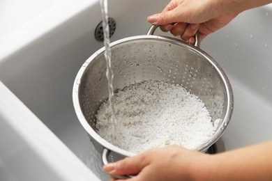 Woman rinsing rice in colander at sink, closeup