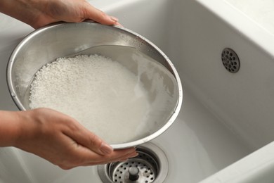 Photo of Woman rinsing rice in bowl above sink, closeup