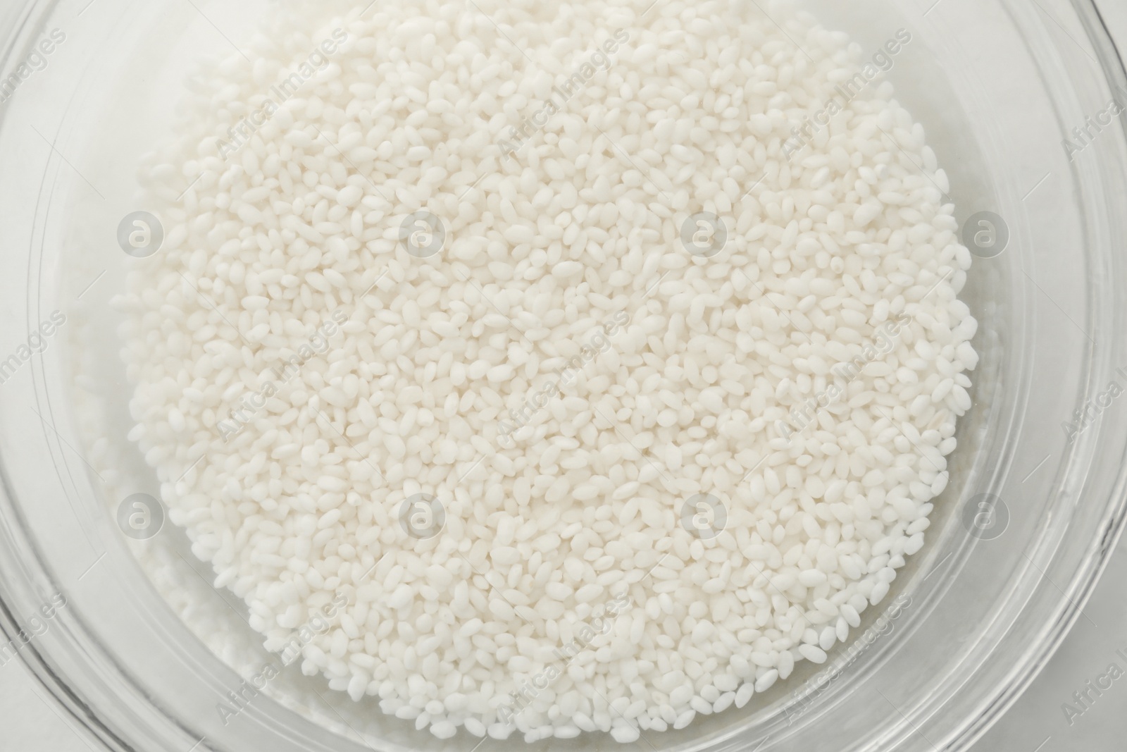 Photo of Raw rice in bowl with water, top view