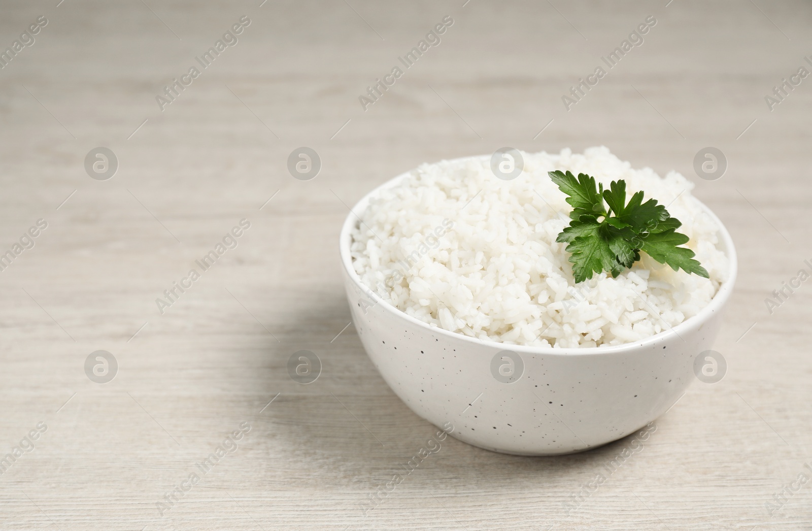 Photo of Delicious boiled rice in bowl and parsley on wooden table, space for text