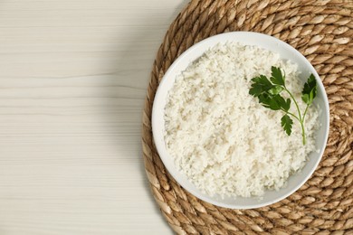 Delicious boiled rice in bowl and parsley on wooden table, top view. Space for text