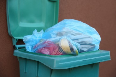 Photo of Trash bags in garbage bin near brown wall outdoors, closeup