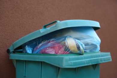 Photo of Trash bags in garbage bin near brown wall outdoors, closeup