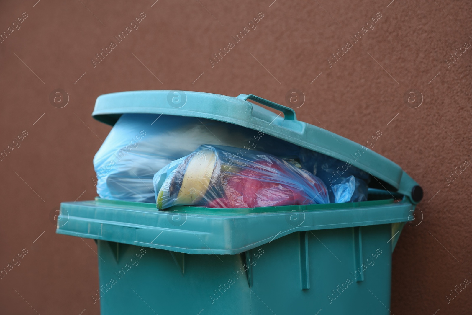 Photo of Trash bags in garbage bin near brown wall outdoors, closeup