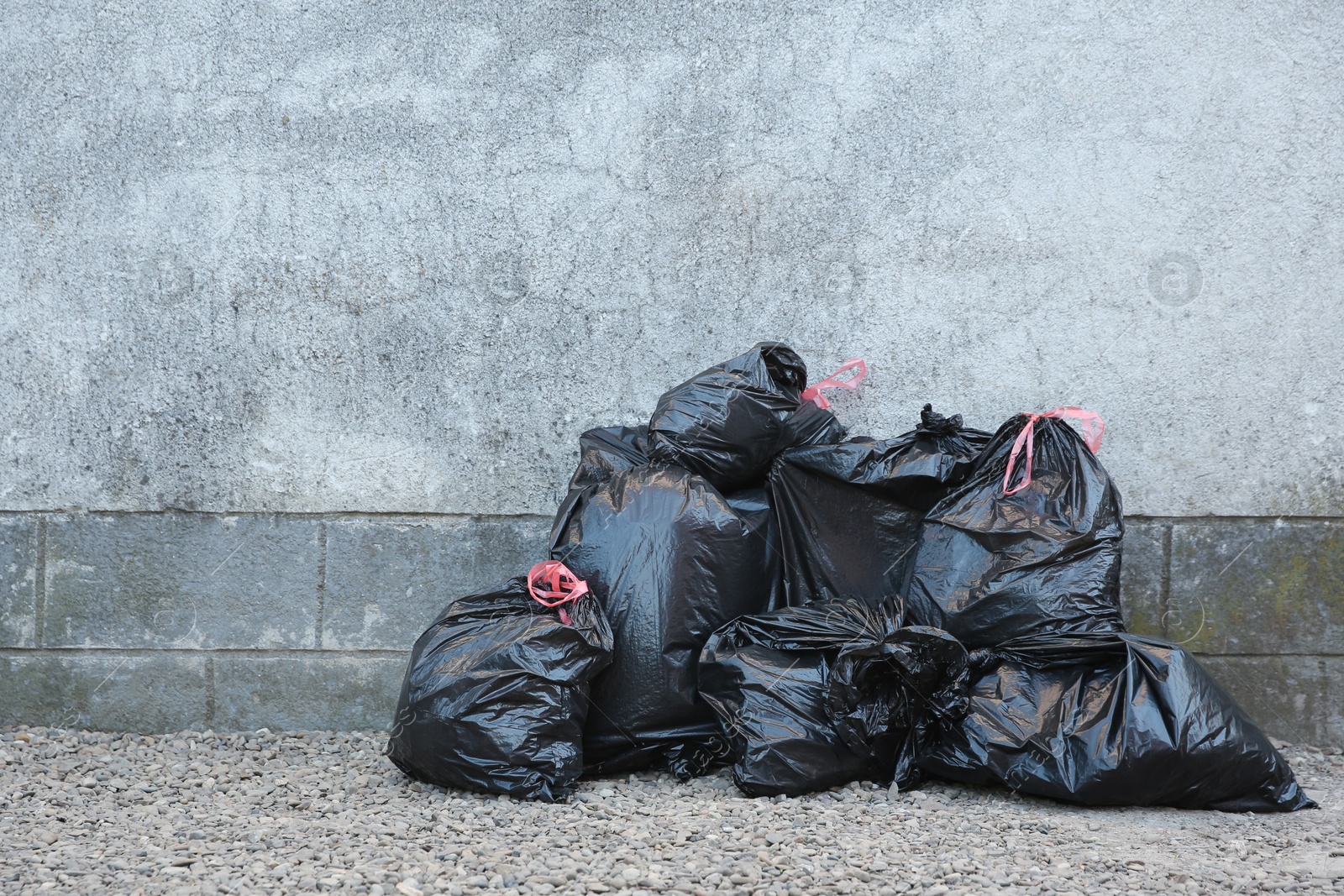 Photo of Many trash bags with garbage near wall outdoors