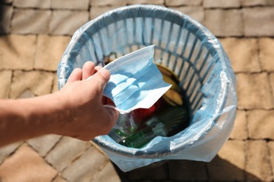 Photo of Man throwing medical mask into garbage bin outdoors, closeup