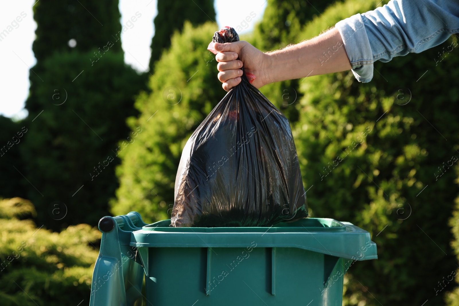 Photo of Man throwing trash bag into bin outdoors, closeup