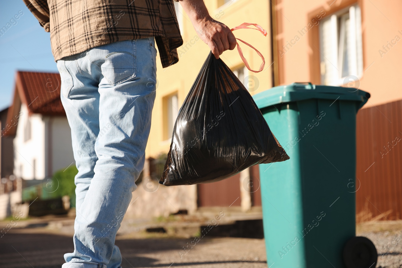 Photo of Man with trash bag full of garbage and bin outdoors, closeup