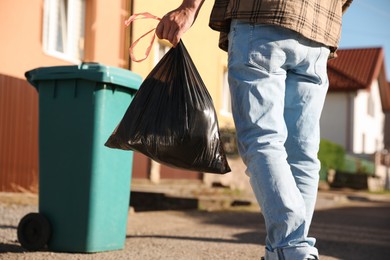 Photo of Man with trash bag full of garbage and bin outdoors, closeup