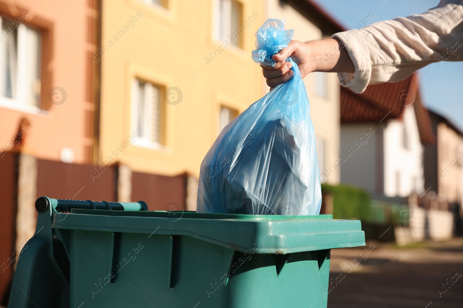 Photo of Man throwing trash bag into bin outdoors, closeup