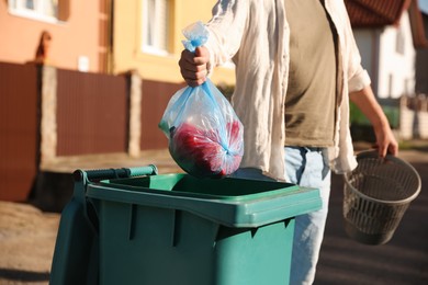 Photo of Man throwing trash bag into bin outdoors, closeup