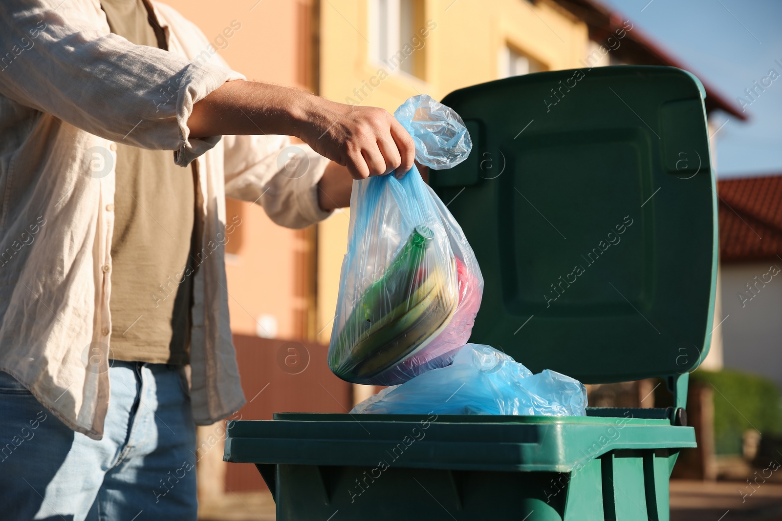 Photo of Man throwing trash bag into bin outdoors, closeup