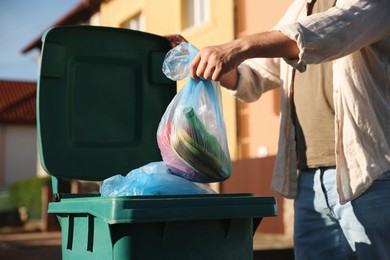 Photo of Man throwing trash bag into bin outdoors, closeup