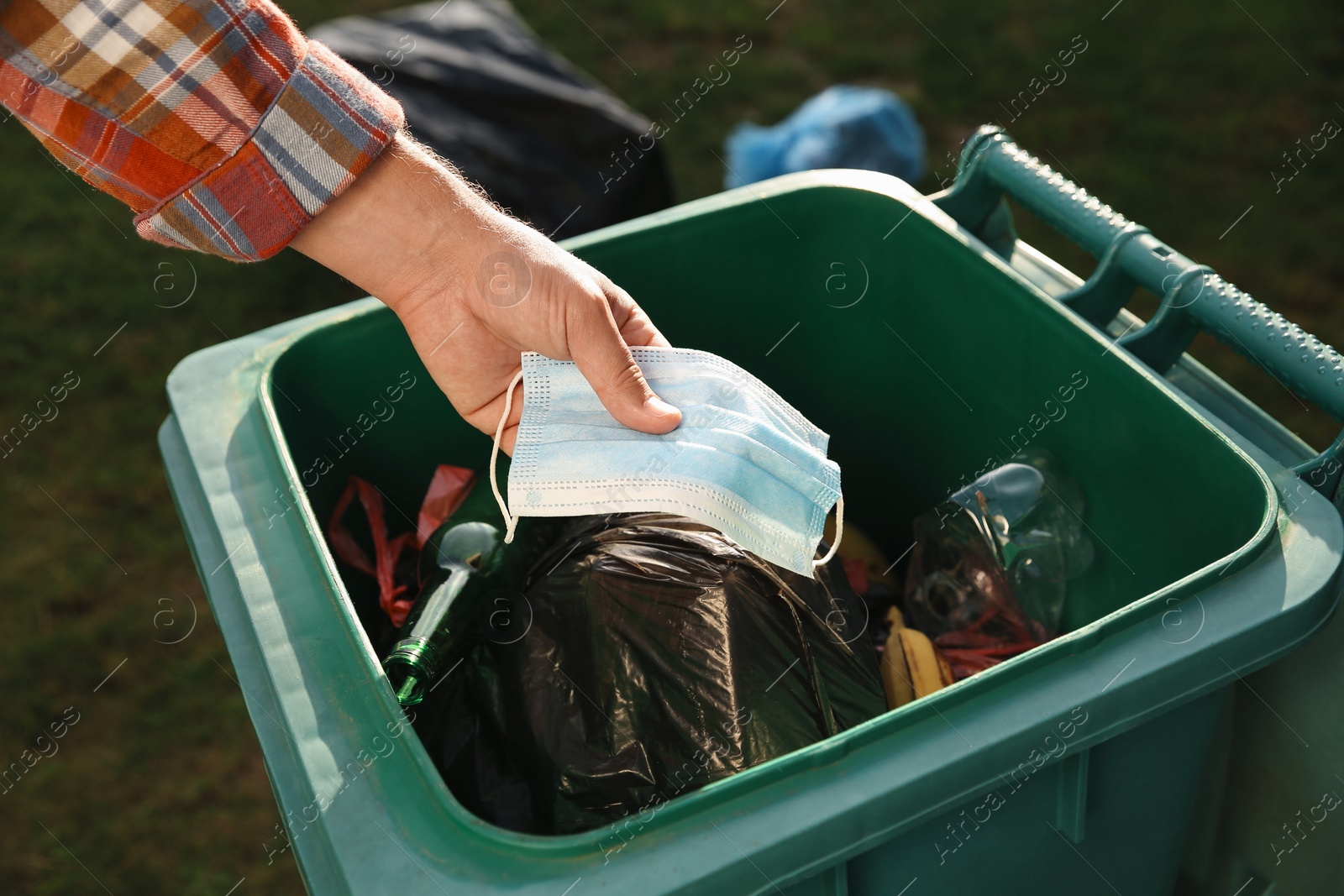 Photo of Man throwing medical mask into garbage bin outdoors, closeup