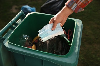 Photo of Man throwing medical mask into garbage bin outdoors, closeup