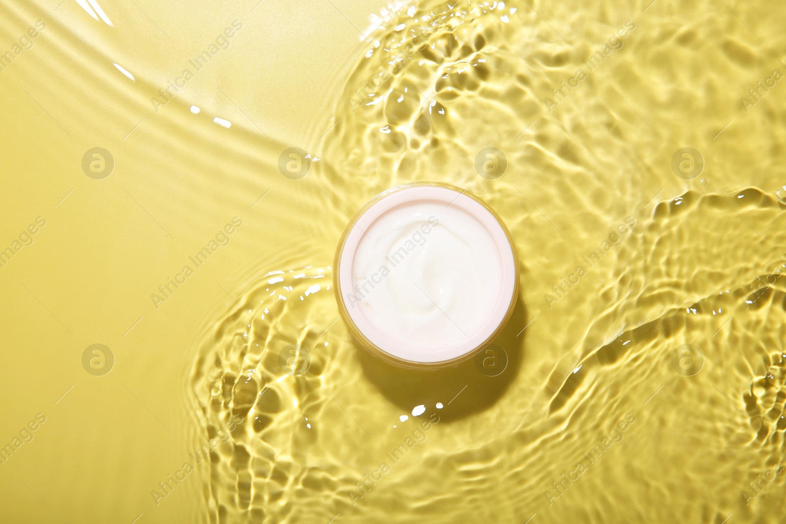 Photo of Jar with cream in water on yellow background, top view. Cosmetic product