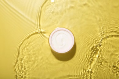 Jar with cream in water on yellow background, top view. Cosmetic product