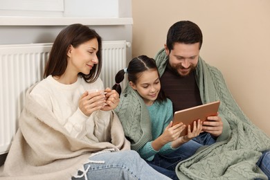 Happy family with tablet near heating radiator at home