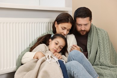 Family with blankets warming near heating radiator at home