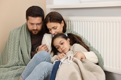 Family with blankets warming near heating radiator at home