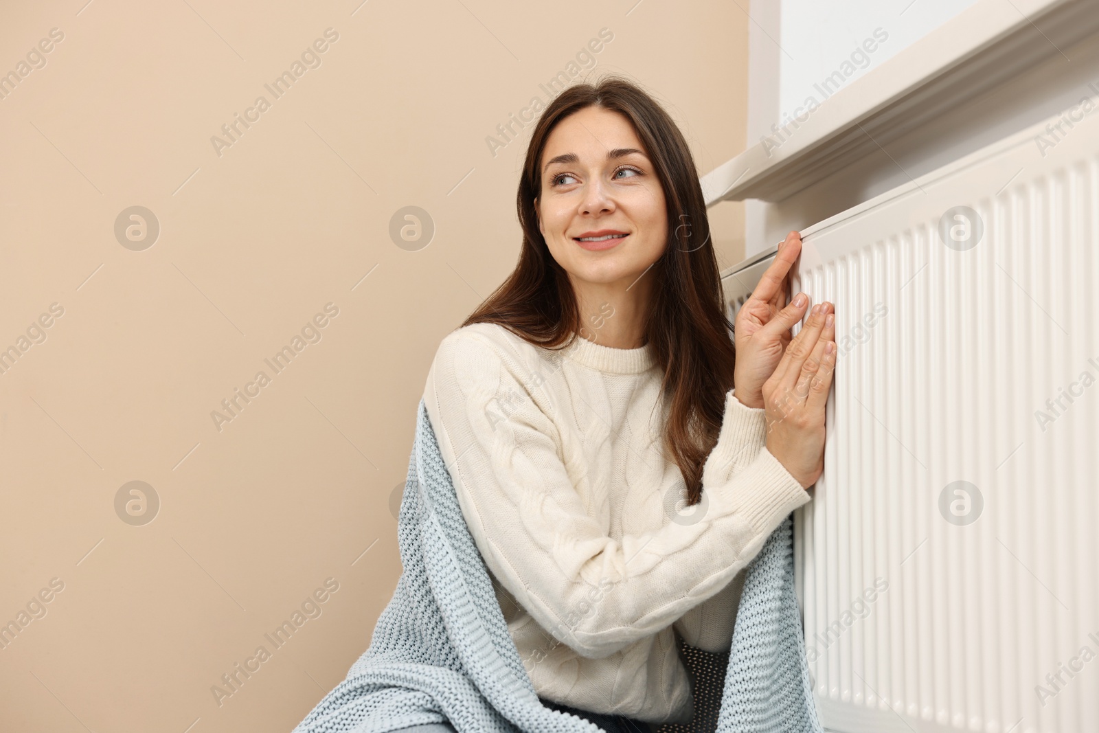 Photo of Woman with blanket warming near heating radiator at home