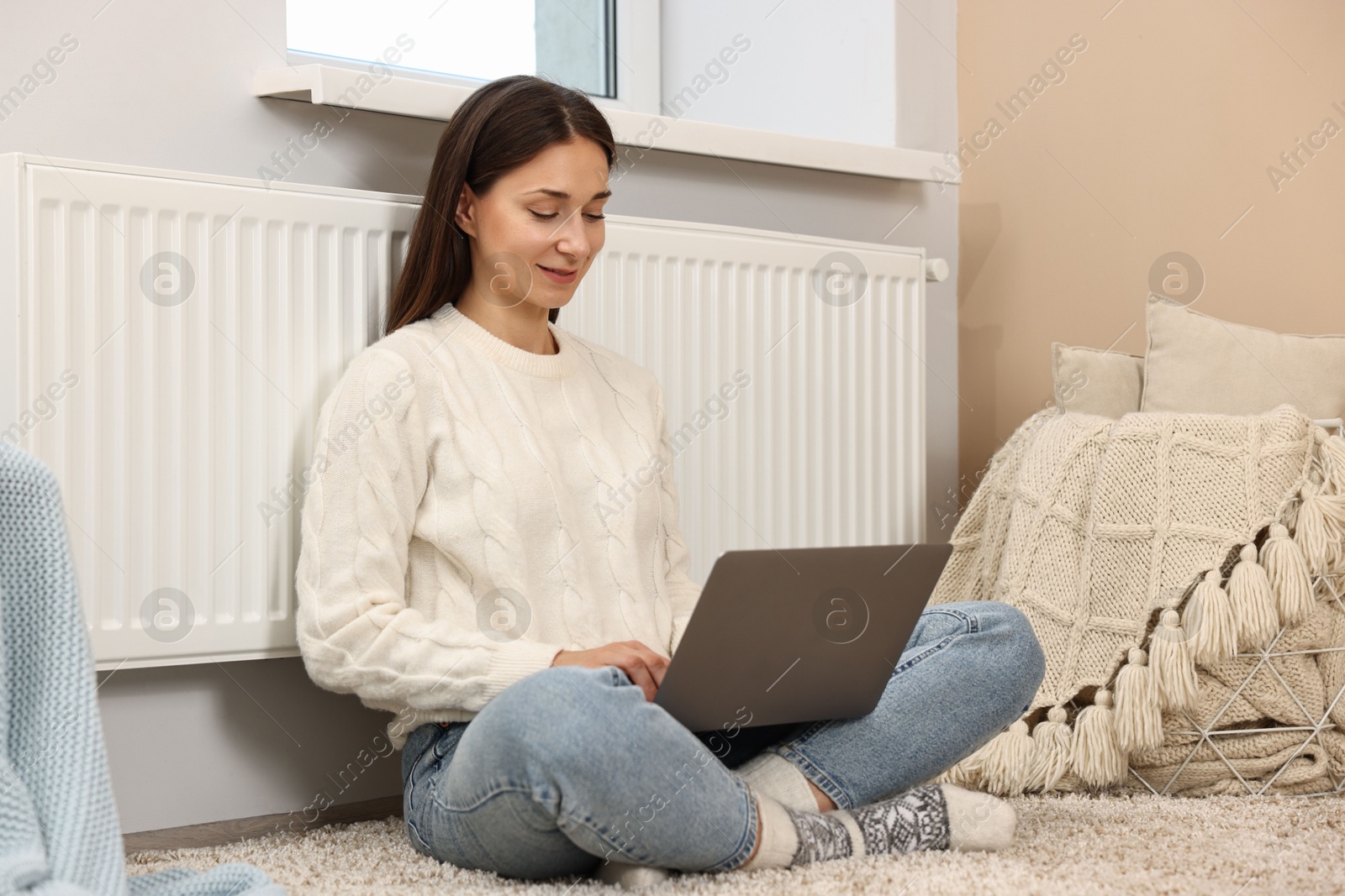 Photo of Happy woman using laptop near heating radiator at home