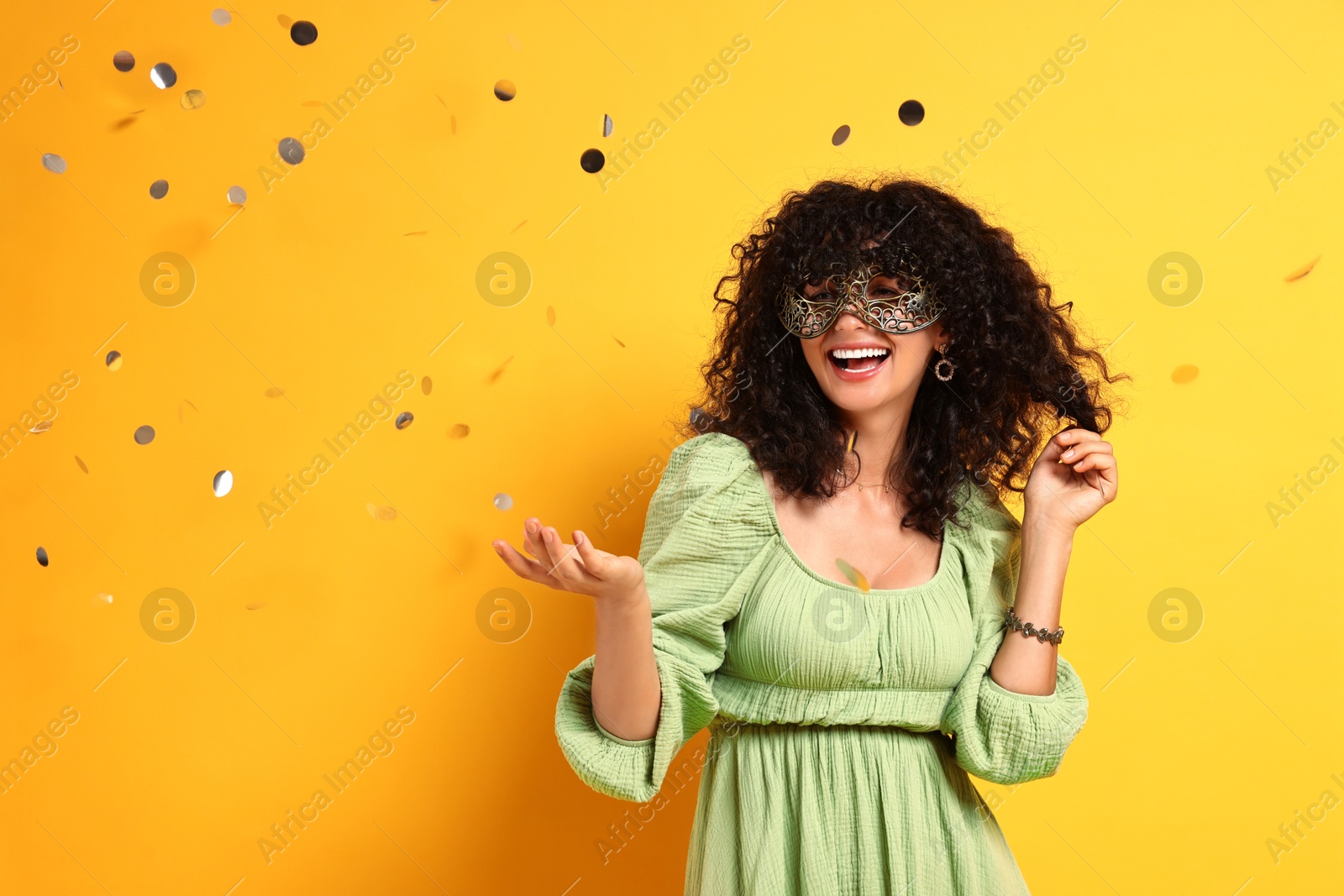 Photo of Happy young woman wearing carnival mask and confetti on yellow background